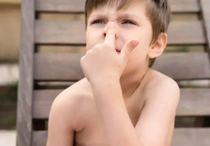 Niño con dedo en la nariz, quizás pensando en comerse los mocos.
