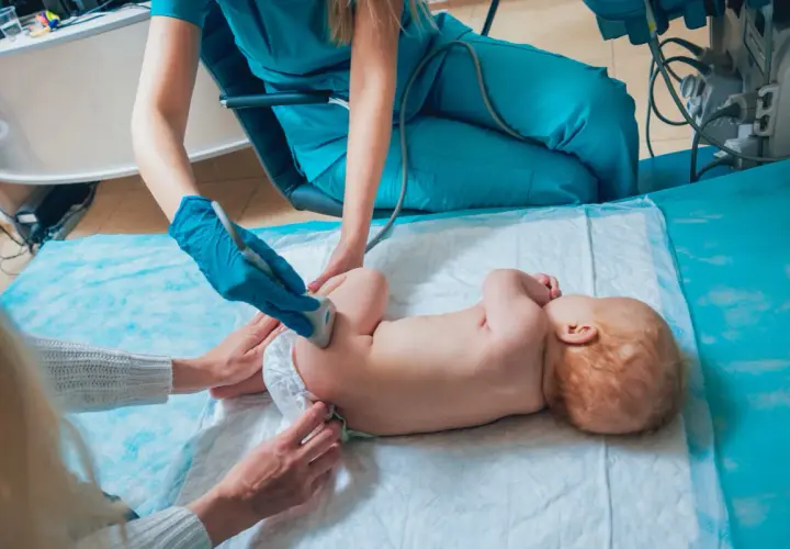 Lekarz wykonuje USG bioderek niemowlaka, sprawdzając, czy nie ma problemów ze strzelającymi stawami.