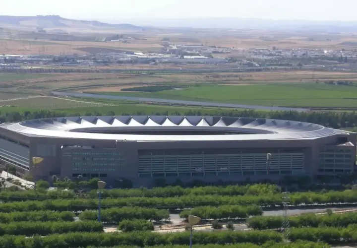 Imponujący stadion La Cartuja otoczony zielenią, z widokiem na pola i miasto w oddali.