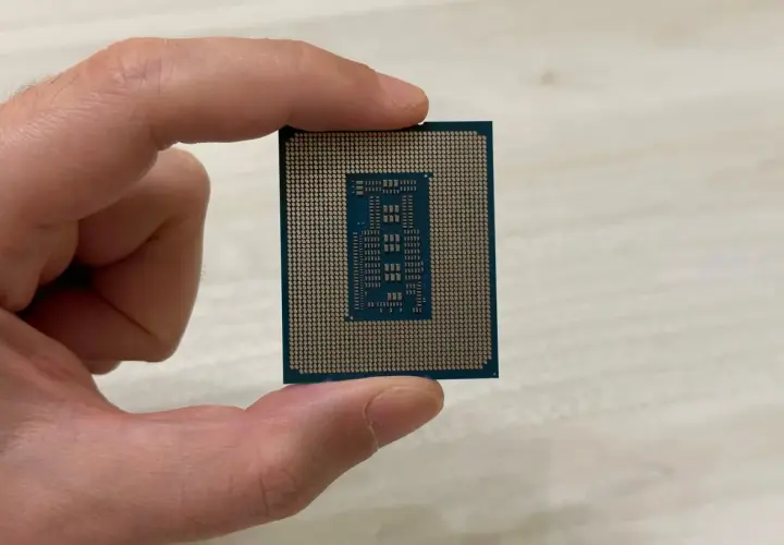 Un dedo sostiene un microprocesador, mostrando su intrincado diseño de pines dorados y el chip central.