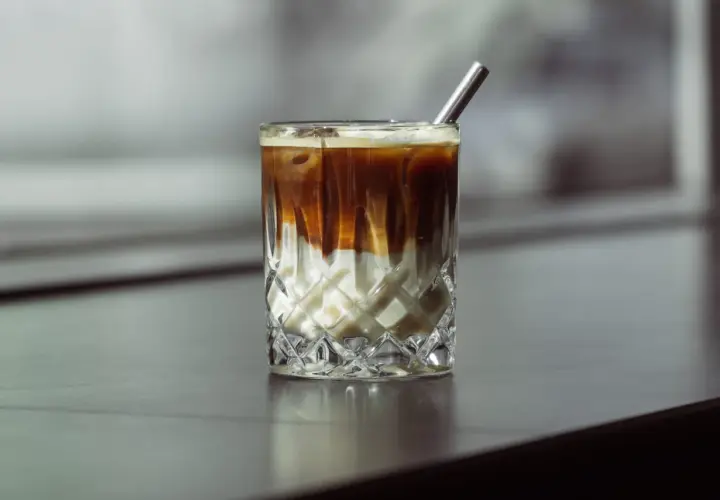 Eiskaffee selber machen ohne Vanilleeis: Ein Glas mit geschichtetem Kaffee und Milch, garniert mit einem Metallstrohhalm.