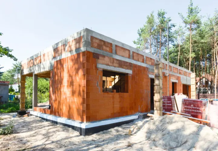 Budowa domu z pustaków ceramicznych. Widać fundamenty, ściany z otworami okiennymi i drzwiowymi. To początek realizacji projektów domów bez pozwolenia.