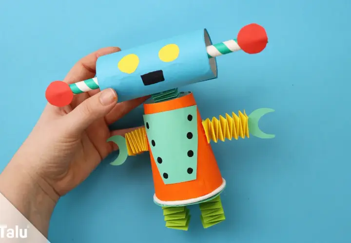 Ein bunter Roboter, der zum **Roboter basteln** einlädt. Er hat einen blauen Kopf mit gelben Augen und einen orangefarbenen Körper.