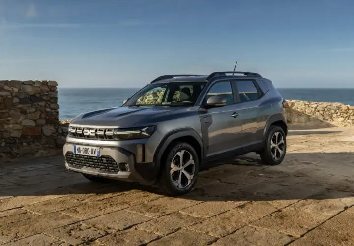 Nowy Dacia SUV na tle kamiennego muru i morza.