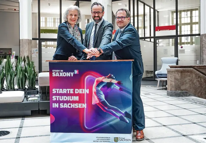 Drei Personen legen ihre Hände auf ein Banner für ein berufsbegleitendes Studium in Leipzig.