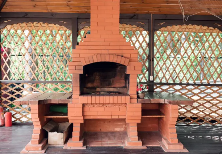 Solidny, prosty grill z cegły w altanie. Obok dwa czerwone gaśnice.