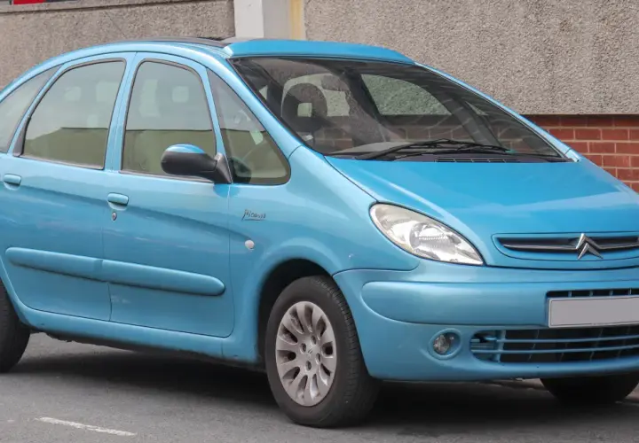 Błękitny Citroen Xsara Picasso z napisem "Picasso" na błotniku, zaparkowany przy ceglanej ścianie.