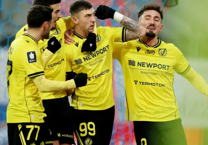 Piłkarze w żółtych koszulkach świętują bramkę. Fani spekulują o plotkach transferowych Widzewa, a drużyna cieszy się sukcesem.