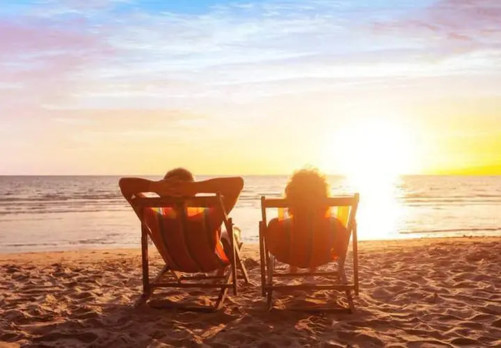 Deux personnes se font dorer la pilule sur des chaises longues, face à un magnifique coucher de soleil sur la mer.
