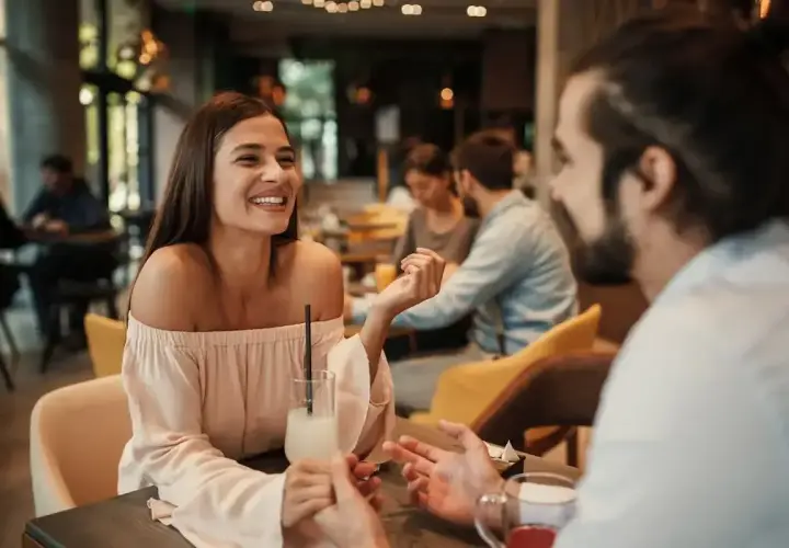 Uśmiechnięta para rozmawia w kawiarni. On zastanawia się, jak zaprosić dziewczynę na wesele.