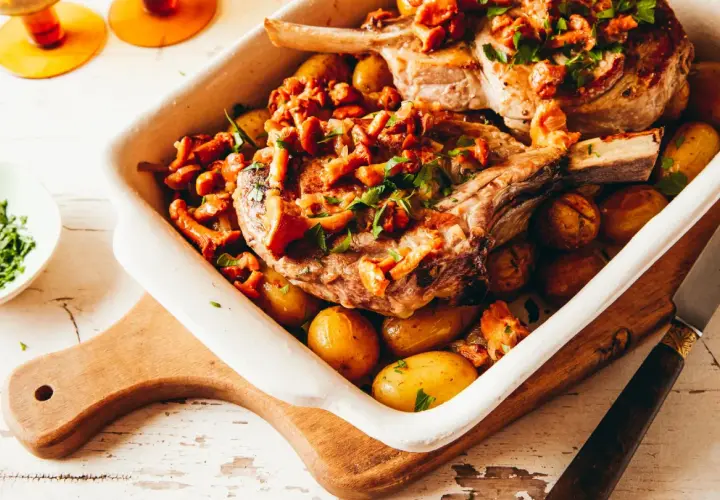 Un plat de viande blanche savoureux, des côtelettes de porc rôties avec des pommes de terre et des girolles, garni de persil frais.