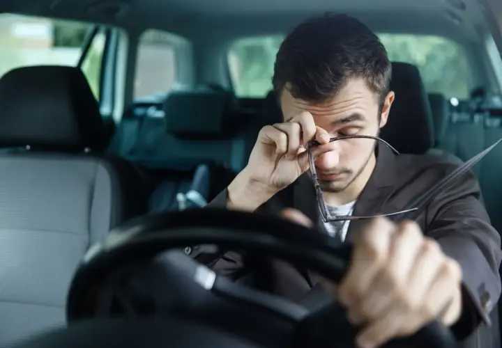 Hombre cansado al volante, se frota los ojos. Para evitar la fatiga en la conducción conviene descansar.