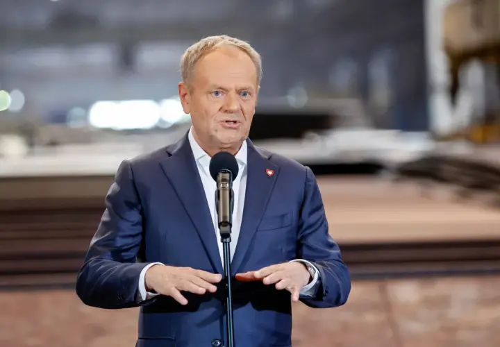 Donald Tusk w garniturze przemawia przy mikrofonie.