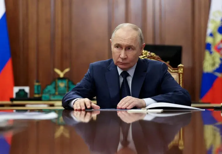 Władimir Putin siedzi przy biurku, zamyślony. Za nim rosyjskie flagi. Czeka na nas świat.