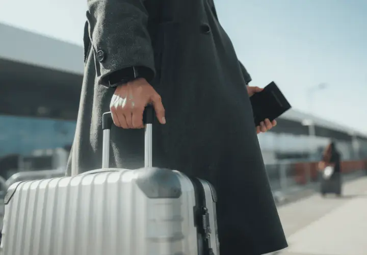 Osoba w płaszczu trzyma walizkę i paszport, gotowa do podróży. W kieszeni czeka karta EKUZ.