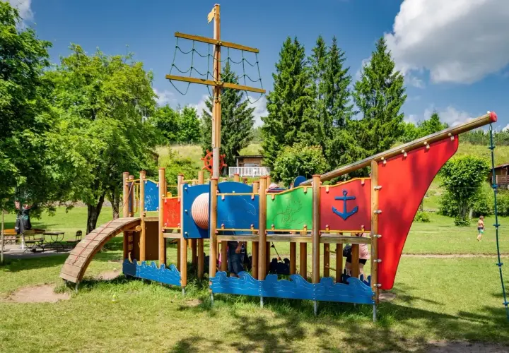 Kolorowy plac zabaw w kształcie statku pirackiego, z drabinkami i zjeżdżalnią, to wspaniałe atrakcje dla dzieci nad brzegiem jeziora.