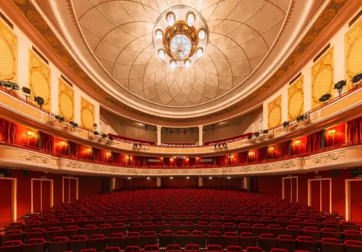 Wnętrze teatru z czerwonymi fotelami i bogato zdobionym sufitem. Czekamy na wspaniały występ.