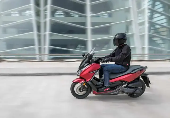 Czerwony skuter z kierowcą w kasku pędzi obok nowoczesnego budynku. To jak tuning 125 na 250, czysta moc!