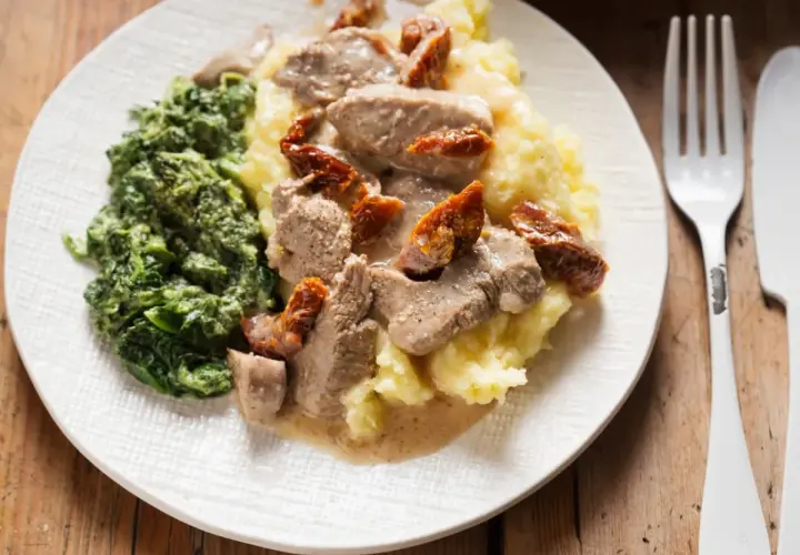 Polędwiczki z suszonymi pomidorami na kremowym purée, obok porcja szpinaku. Pyszny obiad gotowy do podania.