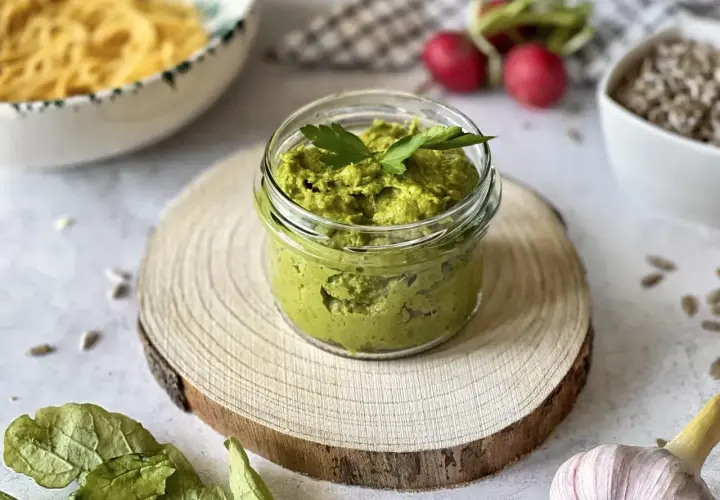 Pesto z liści rzodkiewki w słoiczku, ozdobione natką pietruszki. Obok makaron, rzodkiewki i czosnek.