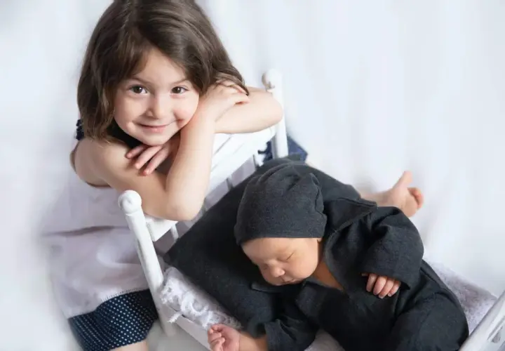 Niña sonríe mientras su hermanito duerme. Quizás ya no habrá rabietas por la llegada de un hermano.