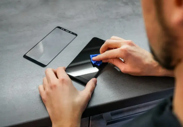 Osoba czyści ekran telefonu przed nałożeniem folii hydrożelowej. Obok leży nowa folia.