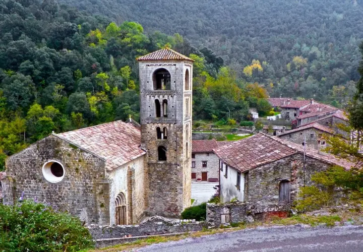 Iglesia románica y casas de piedra en un valle boscoso, ideal para explorar las rutas Camprodon.