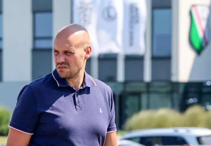 Łysy mężczyzna w granatowej koszulce polo, dyrektor sportowy Legii, patrzy w bok.