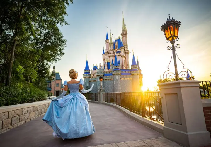 Kopciuszek w błękitnej sukni idzie w stronę zamku w Disneylandzie na Florydzie, podczas zachodu słońca.