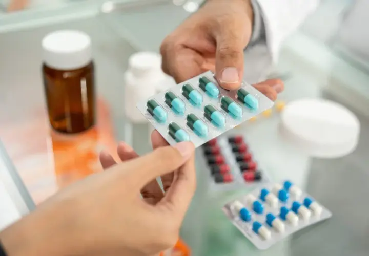 Farmaceuta podaje pacjentowi blistry z lekami, w tym z niebiesko-zielonymi kapsułkami edolox.