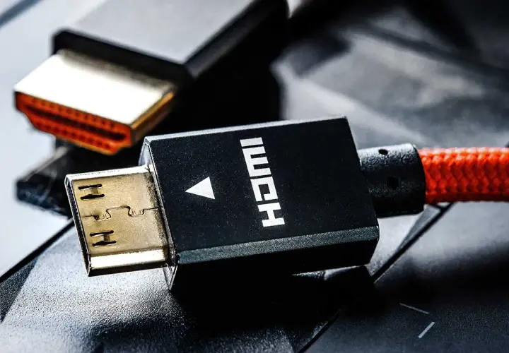 Złote wtyczki HDMI, jedna z nich z czarną obudową i napisem HDMI, połączone z czerwonym, plecionym kablem.