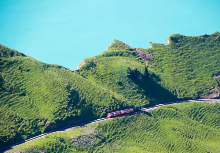 Rött tåg med passagerare på en bergssluttning vid en turkos sjö, en dröm för alla som älskar tåg interrail.