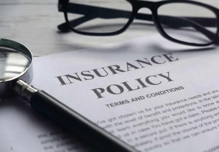 Okulary, lupa i dokument "Insurance Policy" symbolizują analizę polisy PZU po śmierci teścia.
