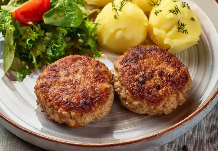Dwa apetyczne kotlety mielone z airfryer, podane z ziemniakami i świeżą sałatką.