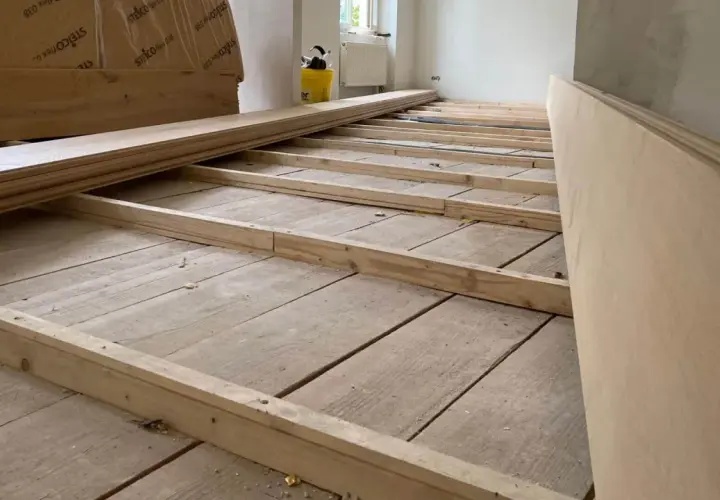 Holzbalken werden auf einem alten Holzboden verlegt, um ihn für neue Bodenplatten vorzubereiten. So kann man den Boden ausgleichen ohne Ausgleichsmasse.