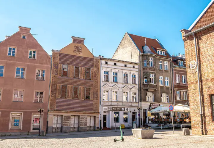 Kamienice Starego Miasta w Olsztynie z widocznym placem i zieloną hulajnogą.