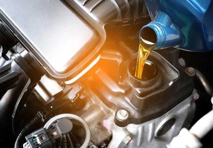 Vertiendo aceite de coche para moto en el motor. El líquido dorado fluye desde un envase azul hacia la abertura de llenado.