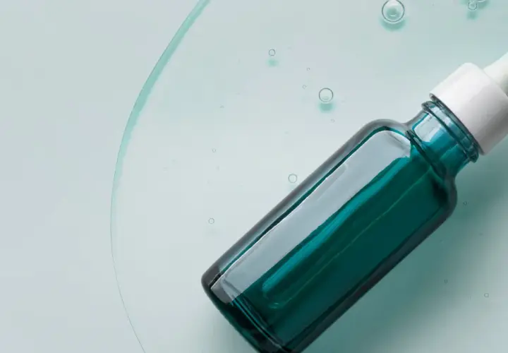 Szklana buteleczka z pipetką, zawierająca serum z kwasem mlekowym, unosząca się w przejrzystej cieczy z bąbelkami.