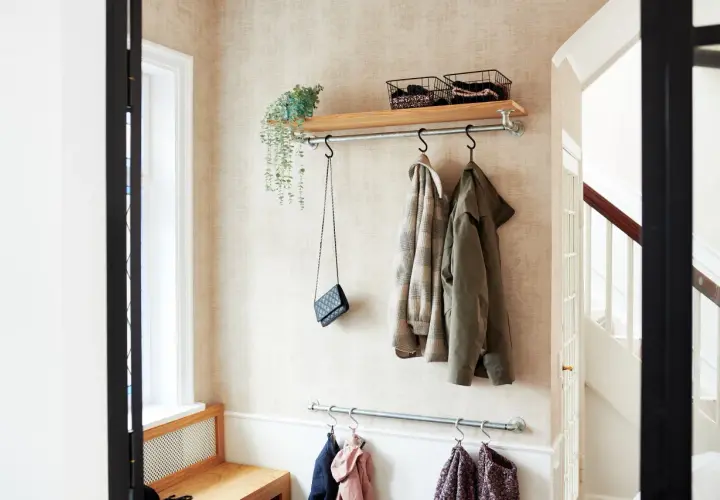 Långsmal hall inspiration med klädhängare, hylla med korgar och en väska. En bänk i trä syns till vänster.