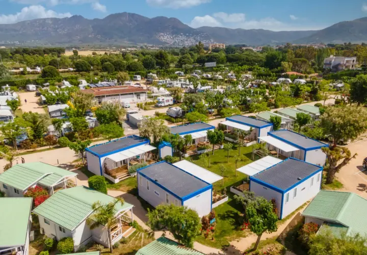 Un complejo de bungalows y caravanas para ir de camping, con montañas al fondo y un cielo azul.