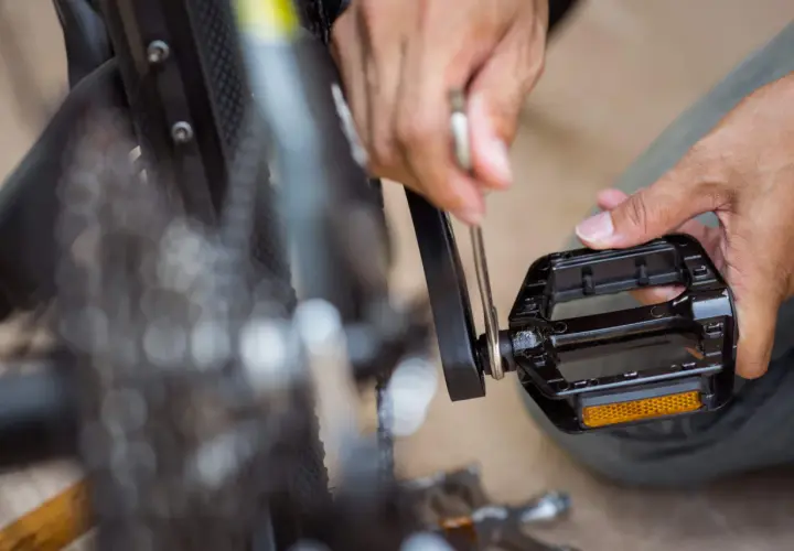 Hände reparieren ein Fahrrad. Ein Werkzeug wird angesetzt, um die Fahrrad Pedale knacken zu beheben.