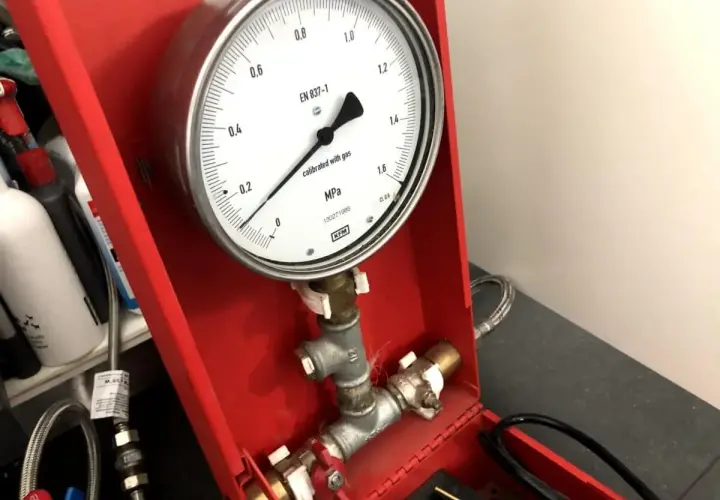 Manometr wskazuje ciśnienie podczas próby szczelności instalacji gazowej. Urządzenie jest częścią czerwonej skrzynki narzędziowej.