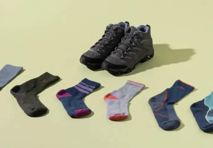 Hiking boots and six pairs of colorful socks are laid out. Is wearing two pairs of socks bad? This image shows options for comfort.