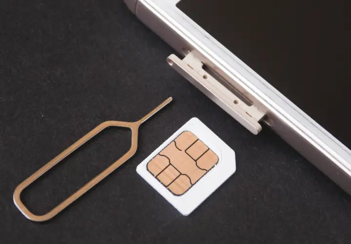 Narzędzie do otwierania tacki SIM i karta SIM obok telefonu. Dowiedz się, jak odblokować kartę SIM, aby móc korzystać z telefonu.