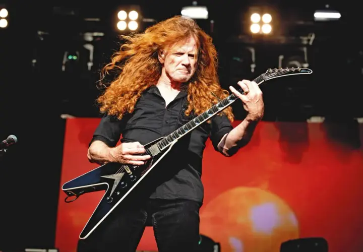 Dave Mustaine z burzą rudych włosów gra na gitarze w kształcie skrzydła.