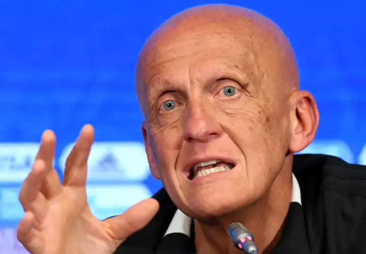 Pier Luigi Collina, znany sędzia piłkarski, przemawia do mikrofonu, gestykulując prawą ręką.