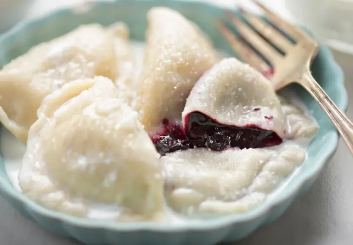 Pyszne pierogi z jagodami, polane śmietaną i posypane cukrem, czekają na widelca.