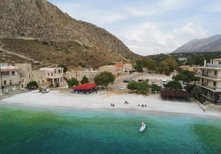 Kamienna plaża i turkusowe morze w Grecji kontynentalnej. W tle kamienne domy i góry. Idealne miejsce na wakacje.