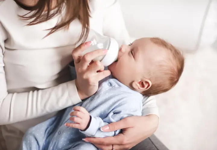 Delikatne karmienie noworodka butelką. Mama trzyma dziecko i podaje mu mleko, pokazując jak karmić noworodka butelką.