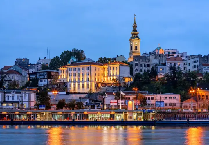 Wieczorny widok na wzgórze z budynkami i kościołem, odbijający się w rzece. Stolica Serbii, Belgrad, prezentuje się malowniczo.